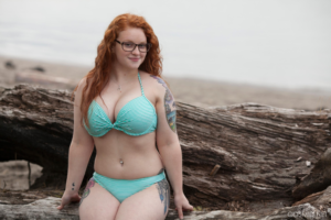 Redhead bikini model sitting on rocks at the beach.