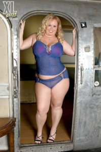 Full figured blonde model in sheer blue cami and panty set standing in the doorway of a vintage airstream travel trailer.